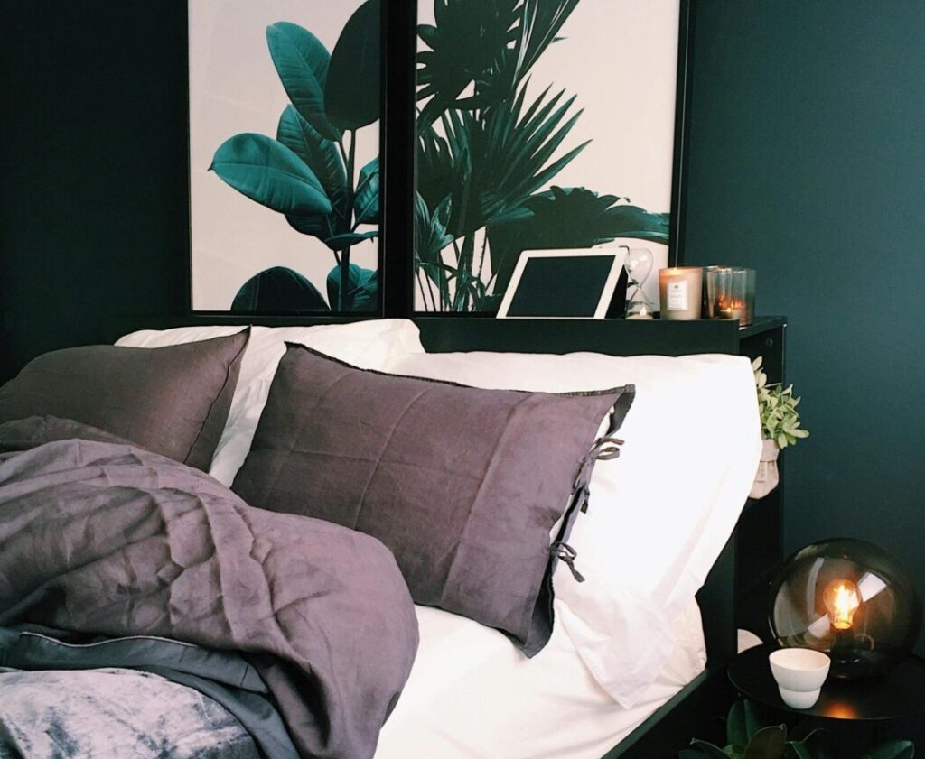 A stylish and cozy bedroom featuring green walls, botanical prints, and soft lighting for a contemporary feel.